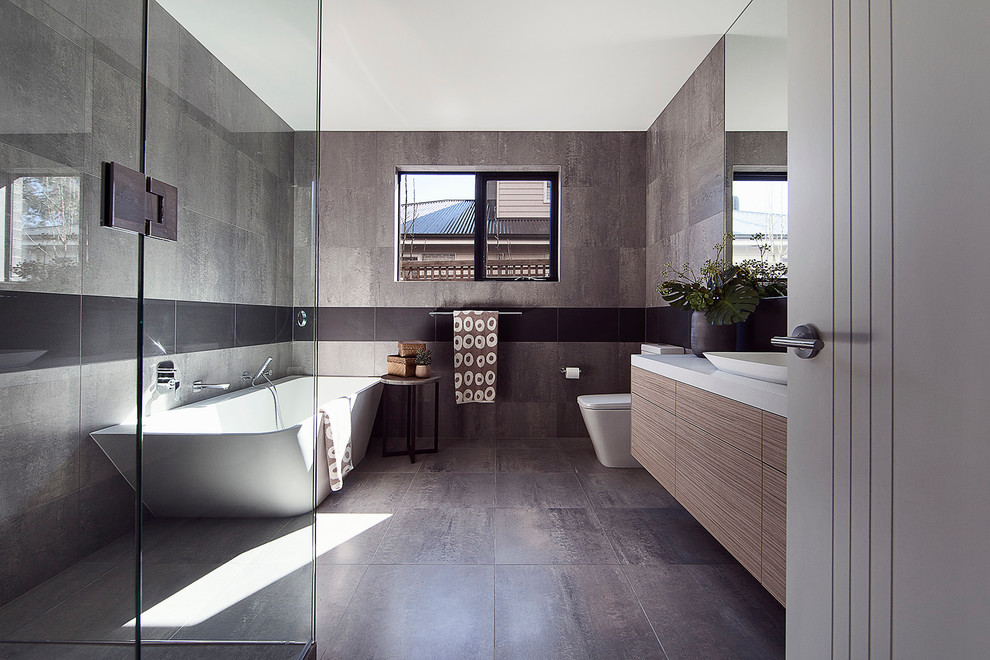 Exemple d'une salle de bain principale moderne en bois brun de taille moyenne avec un lavabo posé, un plan de toilette en quartz modifié, une baignoire indépendante, WC à poser, un carrelage gris, des carreaux de porcelaine, un mur gris, un sol en carrelage de porcelaine et un placard à porte plane.