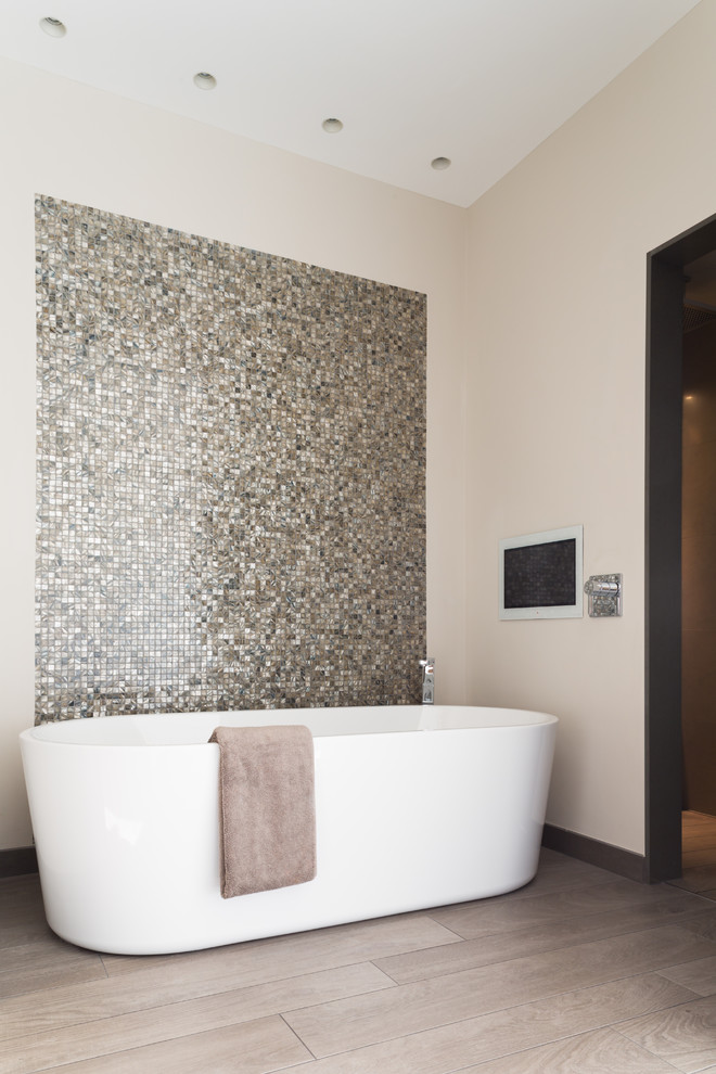 This is an example of a contemporary bathroom in West Midlands with a freestanding bath, mosaic tiles, beige walls, light hardwood flooring and grey tiles.