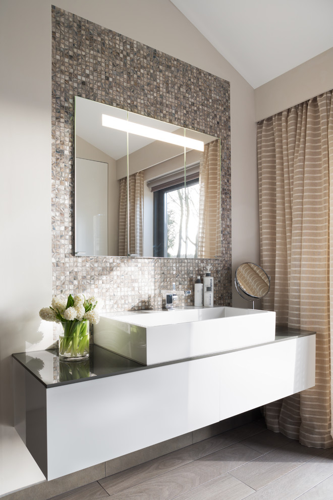 Inredning av ett modernt badrum, med ett fristående handfat, mosaik, beige väggar, klinkergolv i porslin och grå kakel