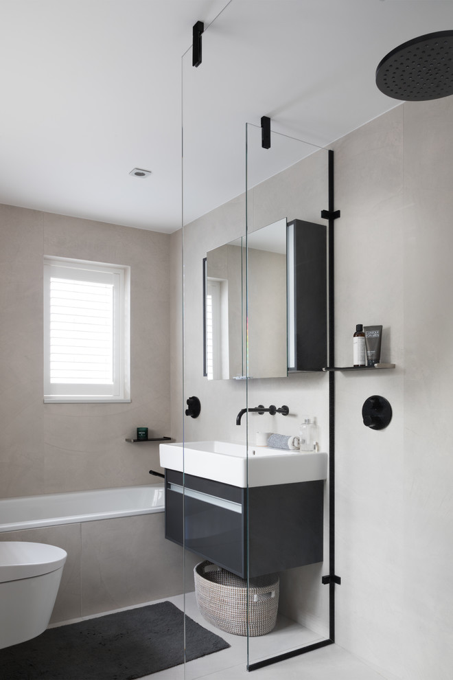 Modern inredning av ett mellanstort en-suite badrum, med släta luckor, ett platsbyggt badkar, grå väggar, ett väggmonterat handfat, grått golv, med dusch som är öppen, våtrum, en vägghängd toalettstol, svarta skåp, stenhäll och betonggolv