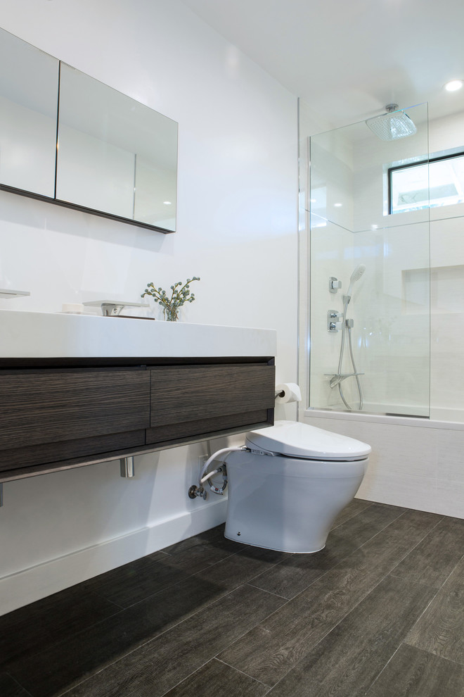Inspiration for a mid-sized contemporary master porcelain tile and gray tile porcelain tile and brown floor tub/shower combo remodel in Los Angeles with an integrated sink, an undermount tub, a one-piece toilet, white walls, flat-panel cabinets, dark wood cabinets and solid surface countertops