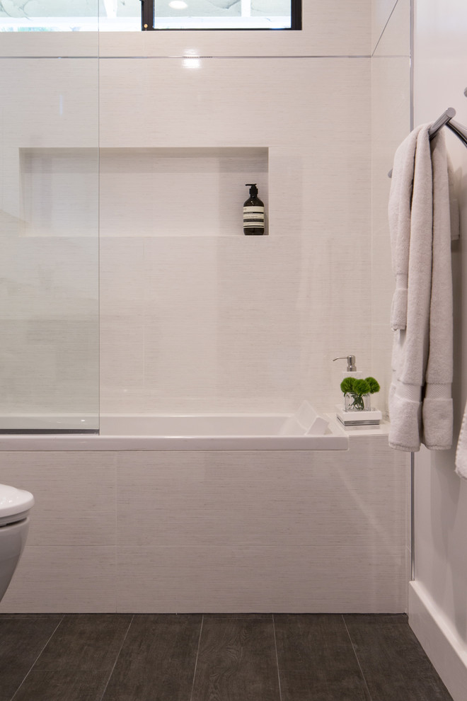 Inredning av ett modernt mellanstort en-suite badrum, med släta luckor, skåp i mörkt trä, bänkskiva i akrylsten, ett undermonterat badkar, en dusch/badkar-kombination, en toalettstol med hel cisternkåpa, grå kakel, porslinskakel, vita väggar, klinkergolv i porslin och brunt golv