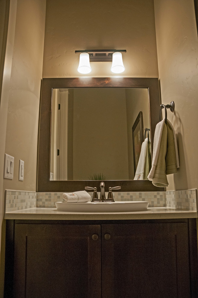 Cette image montre une petite salle de bain traditionnelle en bois brun avec une vasque, un placard avec porte à panneau surélevé, un plan de toilette en quartz, WC à poser, un carrelage gris, un carrelage en pâte de verre, un mur gris et un sol en travertin.