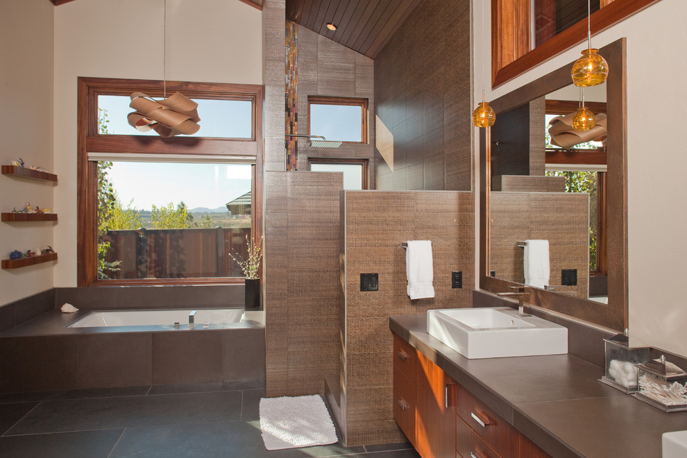 Large trendy master porcelain tile and brown tile slate floor and gray floor corner shower photo in Portland with flat-panel cabinets, medium tone wood cabinets, an undermount tub, a two-piece toilet, beige walls, a vessel sink, solid surface countertops, a hinged shower door and gray countertops
