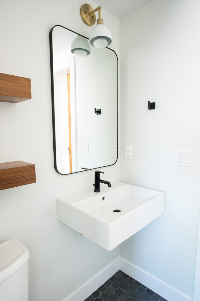 Inredning av ett klassiskt litet badrum, med vita skåp, en kantlös dusch, en toalettstol med separat cisternkåpa, vit kakel, stenkakel, vita väggar, mosaikgolv, ett väggmonterat handfat, svart golv och dusch med gångjärnsdörr