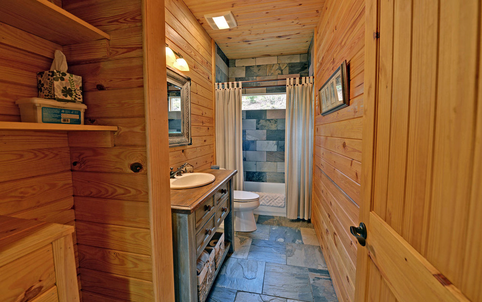 Rustik inredning av ett mellanstort en-suite badrum, med möbel-liknande, skåp i slitet trä, ett badkar i en alkov, en dusch/badkar-kombination, en toalettstol med separat cisternkåpa, flerfärgad kakel, skifferkakel, bruna väggar, skiffergolv, ett nedsänkt handfat, träbänkskiva, flerfärgat golv och dusch med duschdraperi