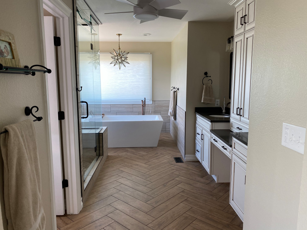 Photo of a large ensuite bathroom in Denver with white cabinets, a freestanding bath, a double shower, a one-piece toilet, grey tiles, porcelain tiles, grey walls, porcelain flooring, a submerged sink, brown floors, a hinged door, black worktops, a wall niche, double sinks and a built in vanity unit.