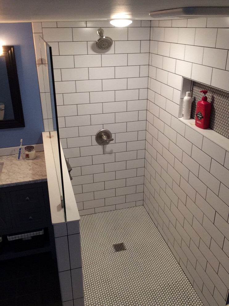 Inredning av ett mellanstort badrum med dusch, med möbel-liknande, blå skåp, en kantlös dusch, vit kakel, tunnelbanekakel, cementgolv, ett konsol handfat, marmorbänkskiva, svart golv och med dusch som är öppen