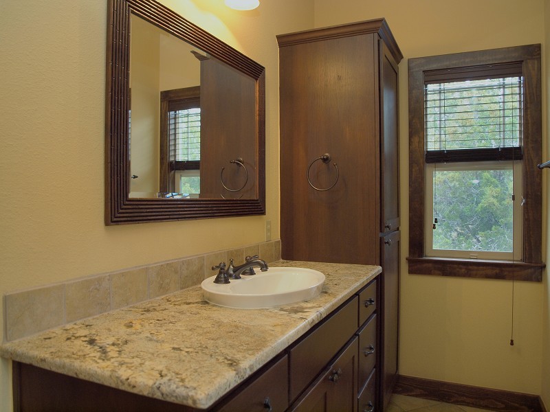 Cette image montre une salle d'eau chalet en bois foncé de taille moyenne avec un placard à porte shaker, un mur beige, un sol en carrelage de céramique, une vasque et un plan de toilette en granite.