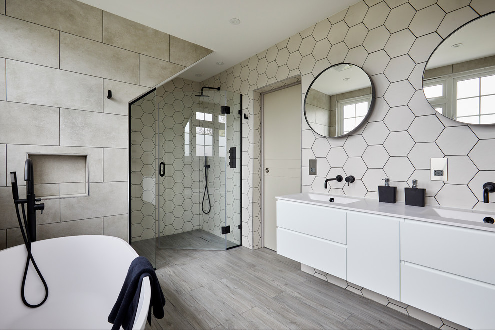 Modernes Badezimmer mit flächenbündigen Schrankfronten, weißen Schränken, freistehender Badewanne, beigen Fliesen, integriertem Waschbecken, grauem Boden und weißer Waschtischplatte in London