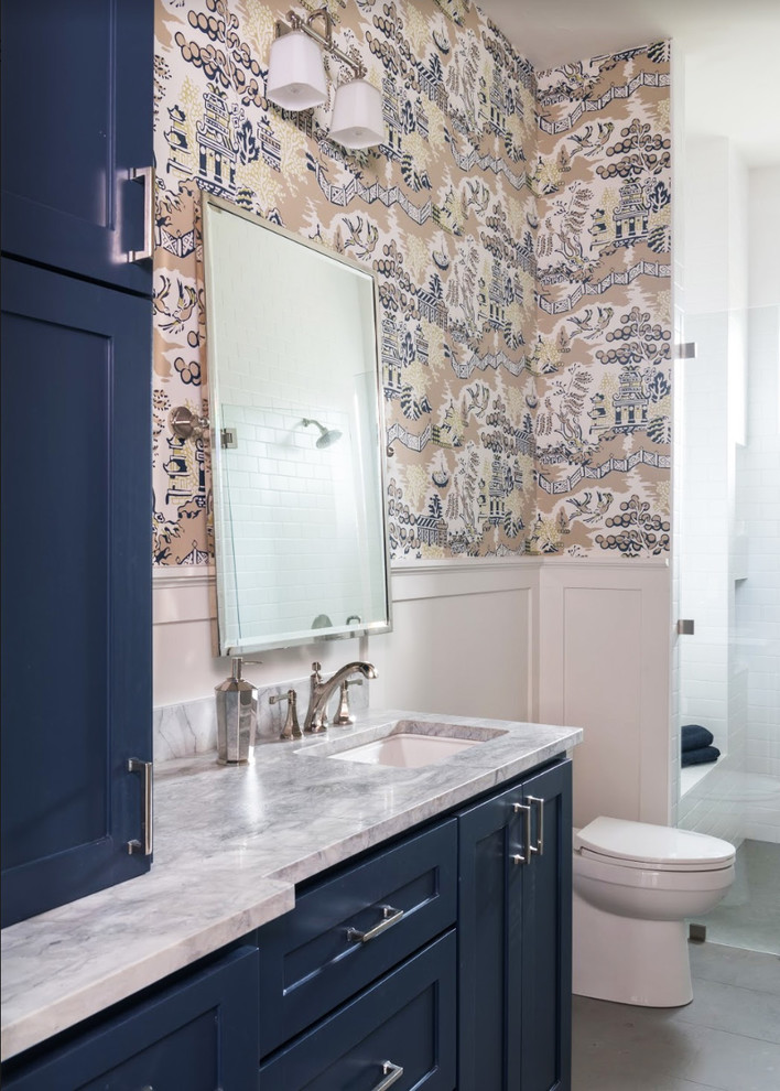 Cette image montre une salle de bain traditionnelle avec un placard à porte shaker, des portes de placard bleues, un mur multicolore, un lavabo encastré, un sol gris, une cabine de douche à porte battante et un plan de toilette blanc.