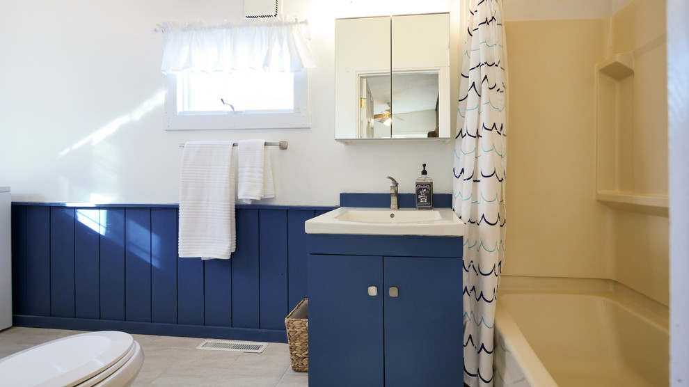 Aménagement d'une salle de bain principale bord de mer de taille moyenne avec un placard à porte plane, des portes de placard bleues, une baignoire posée, un combiné douche/baignoire, WC séparés, un carrelage gris, un sol en carrelage de céramique et un lavabo encastré.
