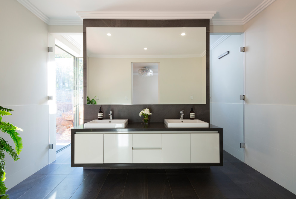 Modern inredning av ett badrum med dusch, med släta luckor, vita skåp, svart kakel, beige väggar, ett fristående handfat och svart golv