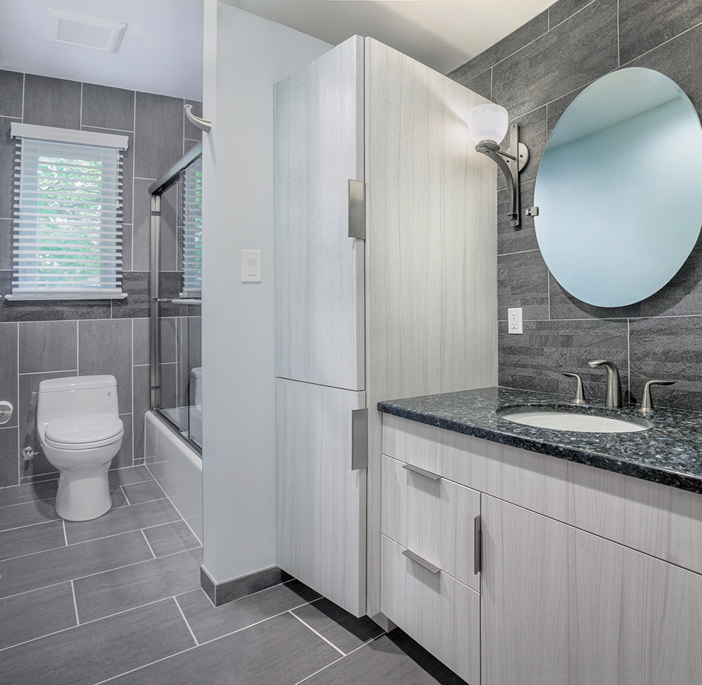 На фото: большая главная ванная комната в современном стиле с плоскими фасадами, серыми фасадами, угловым душем, унитазом-моноблоком, серой плиткой, керамической плиткой, серыми стенами, полом из цементной плитки, накладной раковиной, столешницей из ламината, серым полом, душем с распашными дверями и ванной в нише с