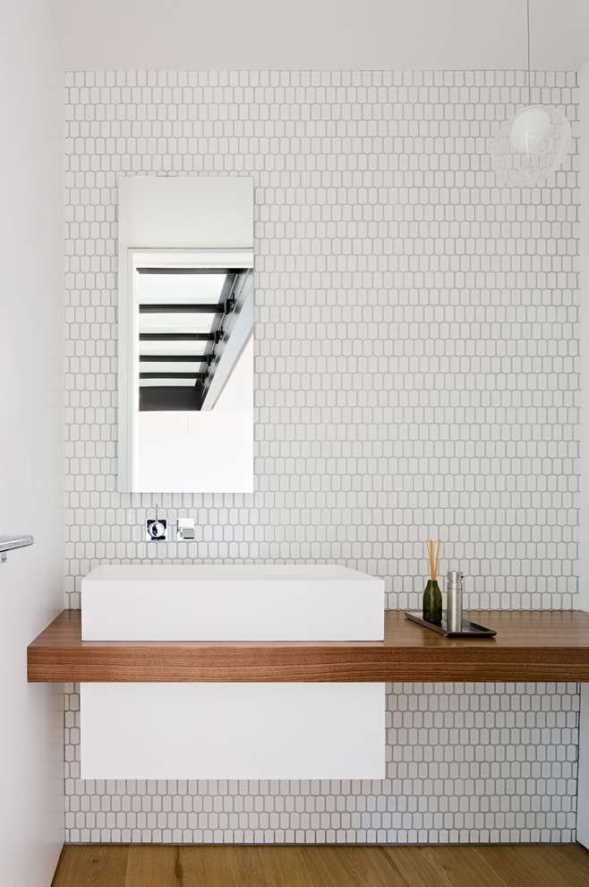 Diseño de cuarto de baño minimalista con paredes blancas, suelo de madera clara, lavabo sobreencimera, encimera de madera, suelo marrón y encimeras marrones