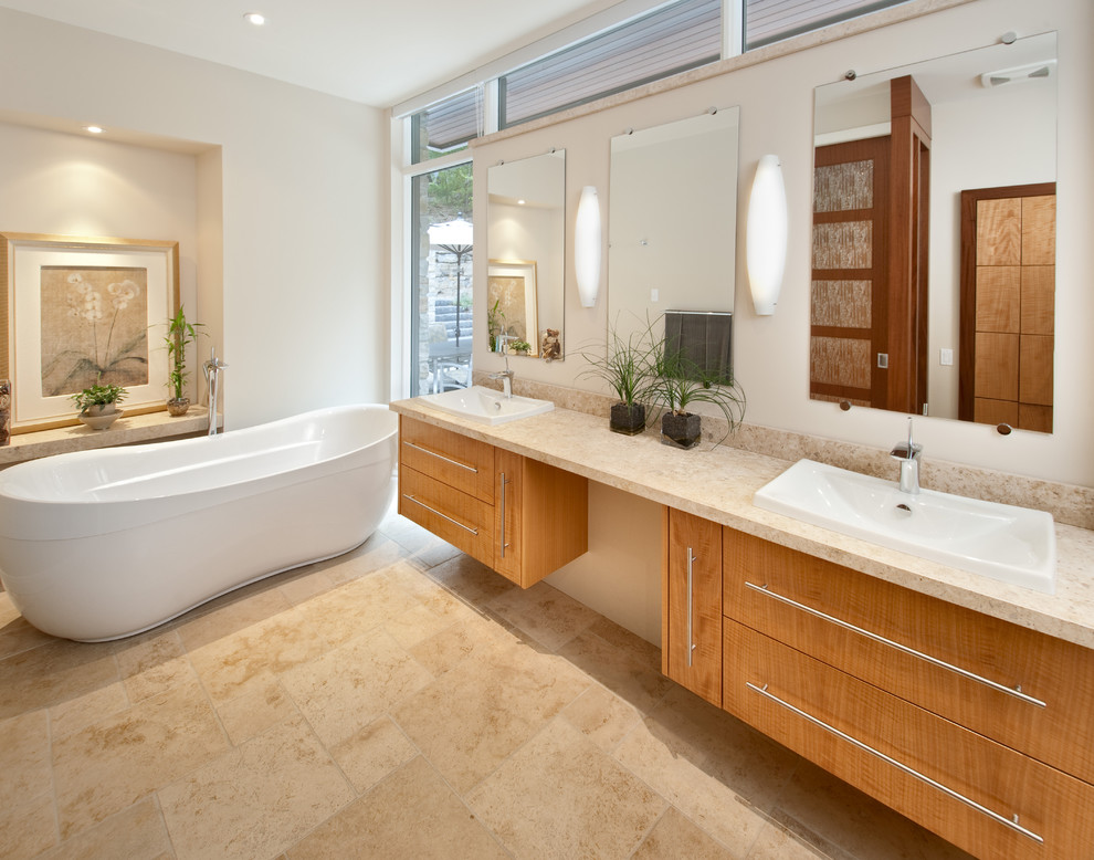Cette photo montre une grande salle de bain principale tendance en bois clair avec un placard à porte plane, une baignoire indépendante, un mur blanc, un sol en calcaire, un lavabo posé, un plan de toilette en granite et un sol beige.