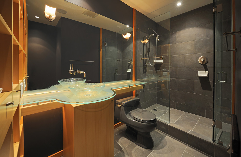 Example of a trendy porcelain tile porcelain tile and gray floor alcove shower design in Vancouver with open cabinets, light wood cabinets, glass countertops, a one-piece toilet, gray walls, a vessel sink and a hinged shower door