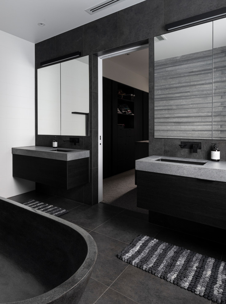 Bild på ett funkis grå grått badrum, med släta luckor, svarta skåp, ett fristående badkar, svart och vit kakel, ett undermonterad handfat och grått golv
