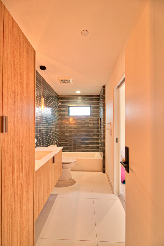 На фото: детская ванная комната среднего размера в стиле модернизм с плоскими фасадами, светлыми деревянными фасадами, ванной в нише, зеленой плиткой, керамической плиткой, врезной раковиной, белым полом, белой столешницей, тумбой под одну раковину и подвесной тумбой с