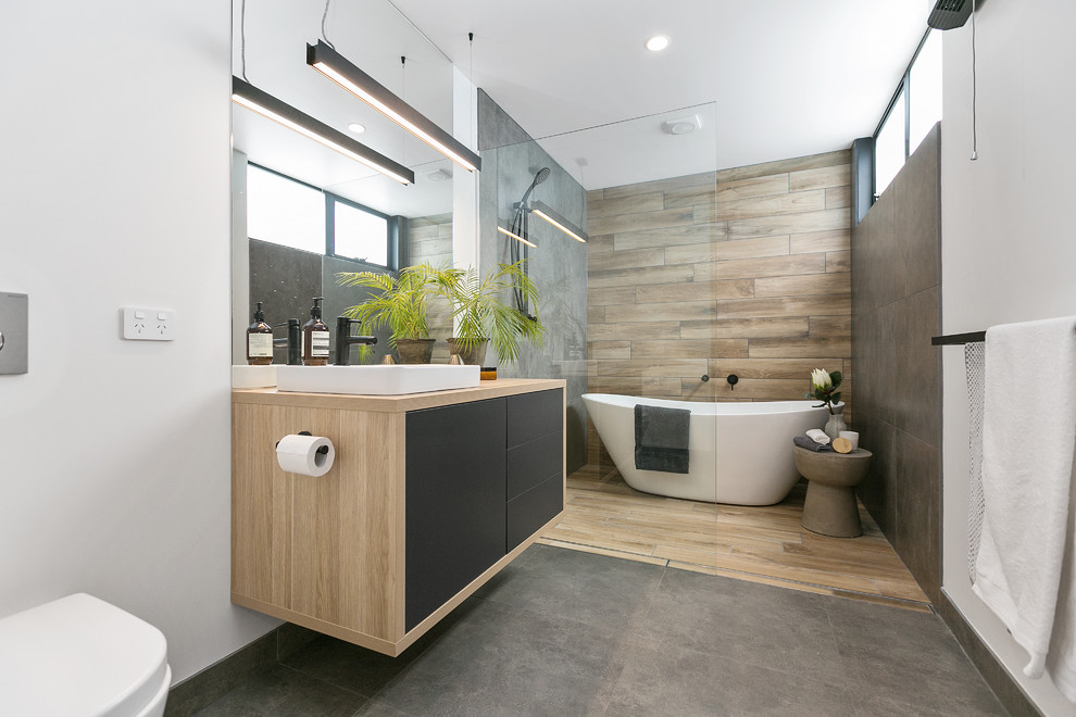 Modern inredning av ett en-suite badrum, med släta luckor, gröna skåp, ett fristående badkar, en kantlös dusch, en vägghängd toalettstol, grå kakel, vita väggar, ett fristående handfat, träbänkskiva, grått golv och med dusch som är öppen