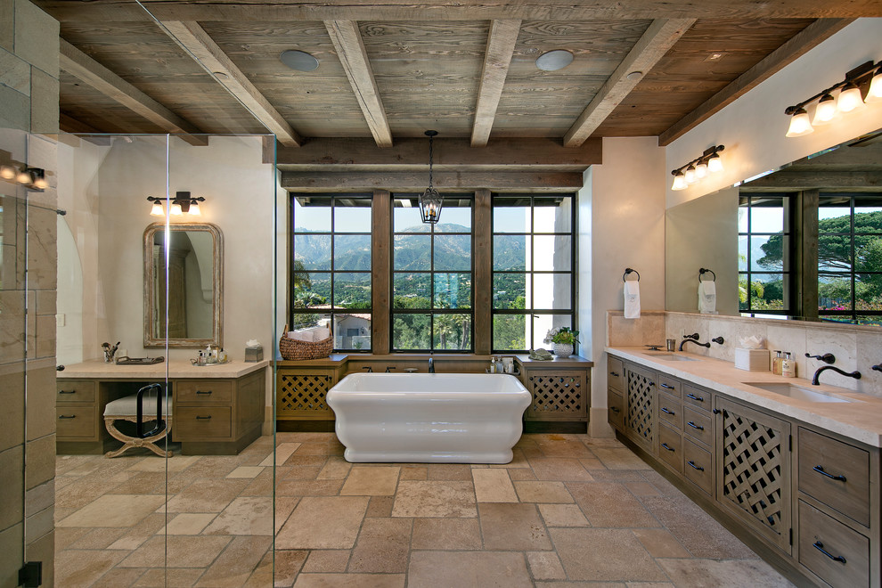 サンタバーバラにある地中海スタイルのおしゃれな浴室 (フラットパネル扉のキャビネット、中間色木目調キャビネット、置き型浴槽、ベージュのタイル、白い壁、アンダーカウンター洗面器、茶色い床、ベージュのカウンター) の写真