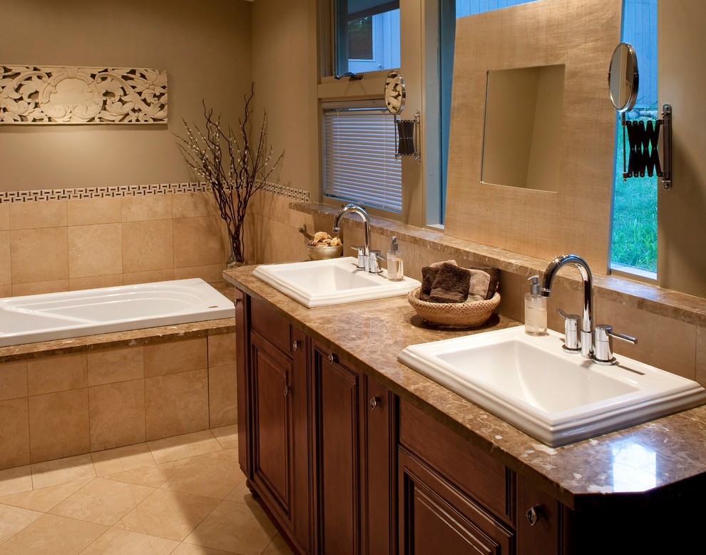 Exemple d'une salle d'eau chic en bois foncé de taille moyenne avec un placard avec porte à panneau surélevé, une baignoire posée, un carrelage beige, des carreaux de céramique, un mur beige, un sol en carrelage de céramique, un lavabo posé, un plan de toilette en marbre et un sol beige.