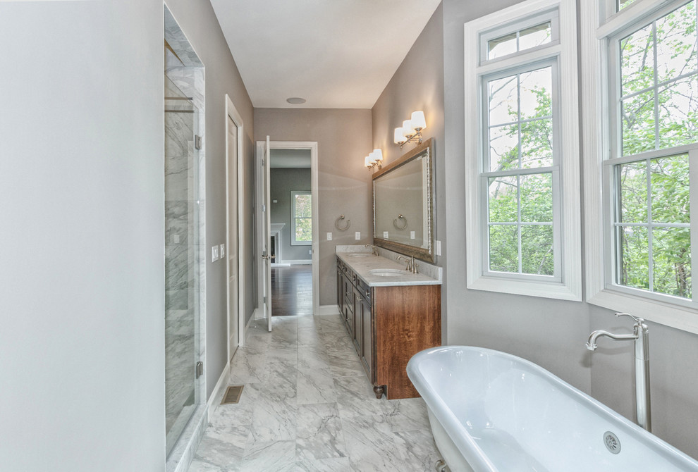 Photo of a large traditional ensuite bathroom in St Louis with recessed-panel cabinets, medium wood cabinets, a claw-foot bath, an alcove shower, a two-piece toilet, grey walls, marble flooring, a submerged sink, marble worktops, grey floors and a hinged door.