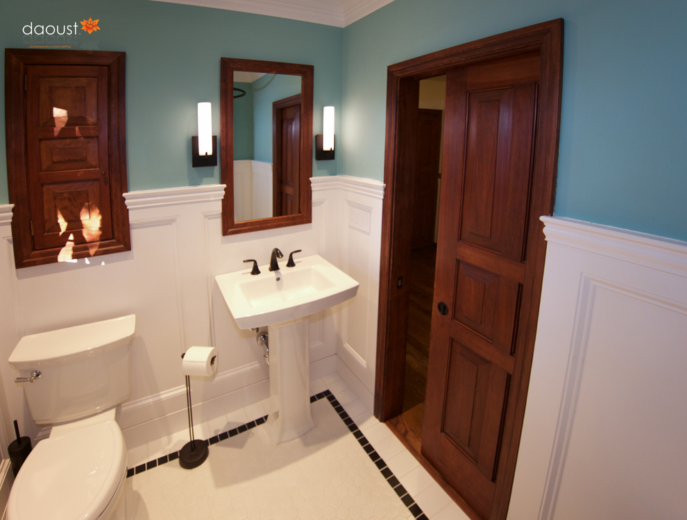 Amerikansk inredning av ett litet badrum, med ett piedestal handfat, luckor med infälld panel, skåp i mörkt trä, en toalettstol med separat cisternkåpa, vit kakel, porslinskakel, blå väggar och mosaikgolv