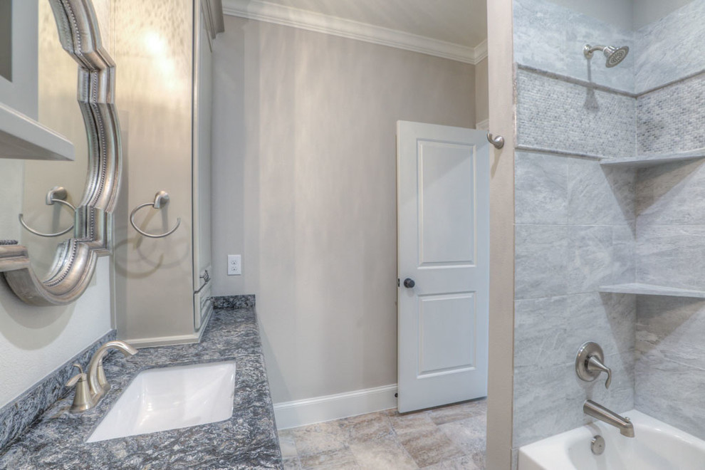 This is an example of a medium sized traditional shower room bathroom in Houston with raised-panel cabinets, grey cabinets, a shower/bath combination, a two-piece toilet, beige tiles, stone tiles, beige walls, porcelain flooring, a submerged sink, granite worktops, beige floors and a shower curtain.