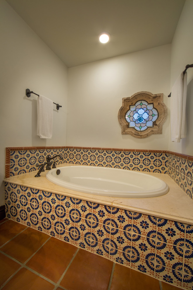 Immagine di una stanza da bagno con doccia mediterranea di medie dimensioni con vasca da incasso, piastrelle in terracotta, pareti bianche, pavimento in terracotta, top in granito e piastrelle multicolore
