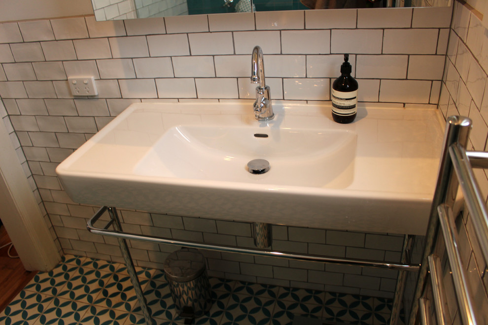 Photo of a small contemporary ensuite bathroom in Melbourne with a pedestal sink, flat-panel cabinets, white cabinets, a built-in shower, white tiles, cement tiles, white walls and ceramic flooring.