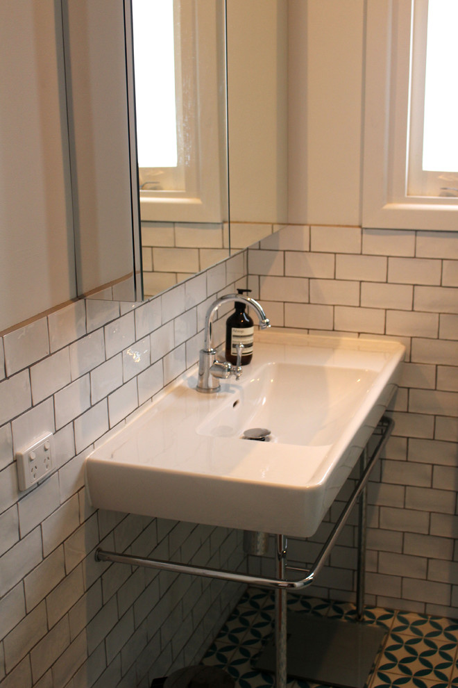 Modern inredning av ett litet en-suite badrum, med ett piedestal handfat, släta luckor, en kantlös dusch, vit kakel, vita väggar och klinkergolv i keramik
