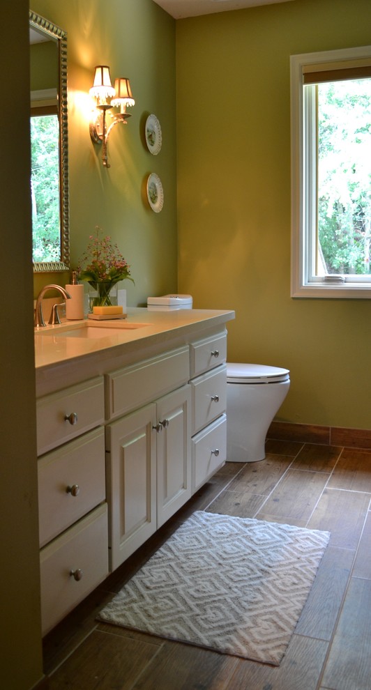 Klassisk inredning av ett mellanstort en-suite badrum, med luckor med upphöjd panel, vita skåp, gröna väggar, mellanmörkt trägolv, ett undermonterad handfat, bänkskiva i akrylsten, ett badkar i en alkov och en dusch/badkar-kombination