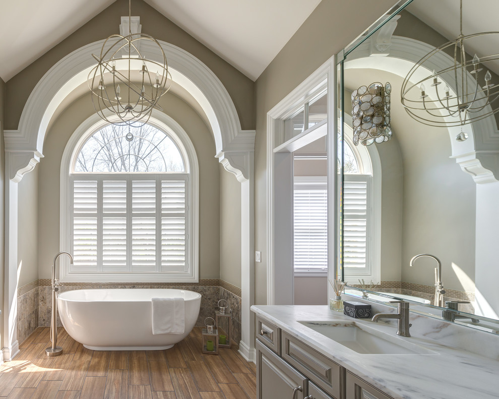 Пример оригинального дизайна: ванная комната в классическом стиле с врезной раковиной, фасадами с выступающей филенкой, серыми фасадами, отдельно стоящей ванной, серыми стенами и паркетным полом среднего тона