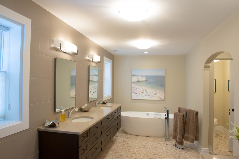 Cette photo montre une salle de bain chic avec un lavabo encastré, un placard à porte plane, des portes de placard marrons, un plan de toilette en marbre, une baignoire indépendante, une douche d'angle, WC séparés, un carrelage beige, une plaque de galets, un mur noir et un sol en galet.