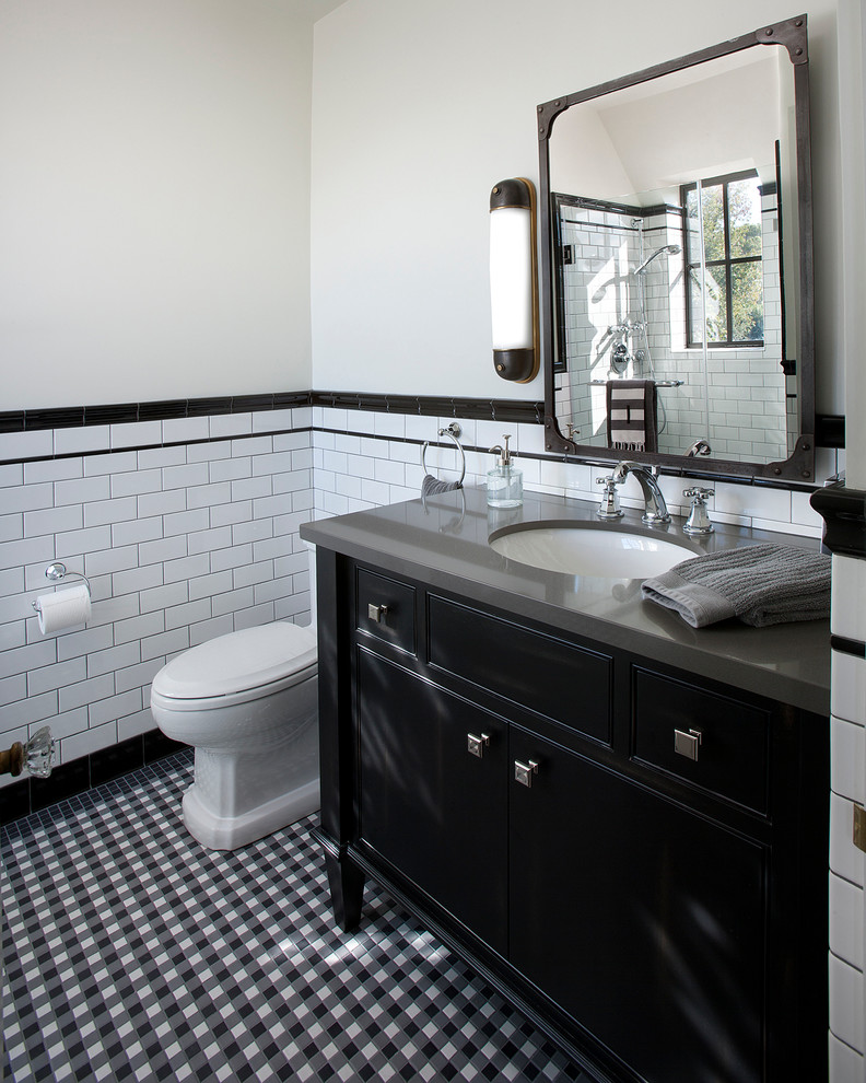 Cette image montre une salle de bain traditionnelle avec un lavabo encastré, des portes de placard noires, un carrelage métro, un mur blanc, un carrelage noir et blanc, un plan de toilette gris, du carrelage bicolore et un placard à porte affleurante.