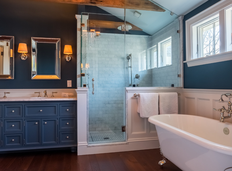 Idée de décoration pour une salle de bain principale tradition avec un placard à porte shaker, des portes de placard bleues, une baignoire sur pieds, une douche d'angle, un mur bleu, parquet foncé, un lavabo encastré et un plan de toilette en marbre.