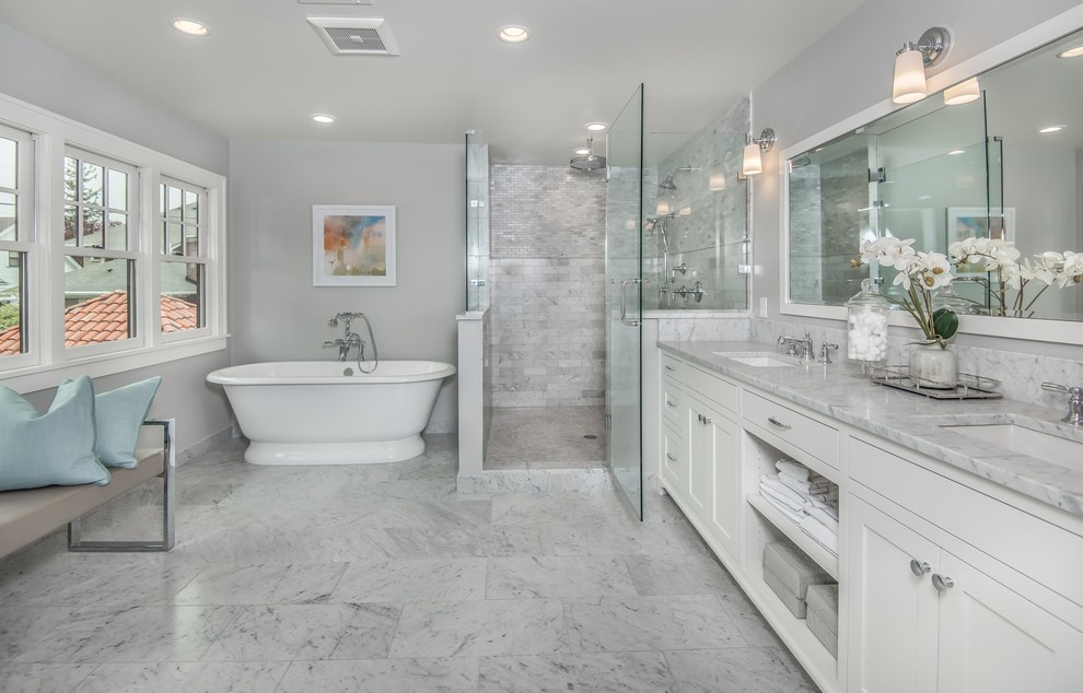 Klassisk inredning av ett mycket stort en-suite badrum, med luckor med infälld panel, vita skåp, ett fristående badkar, en dubbeldusch, en toalettstol med hel cisternkåpa, grå kakel, marmorkakel, grå väggar, marmorgolv, ett undermonterad handfat, marmorbänkskiva, grått golv och dusch med gångjärnsdörr