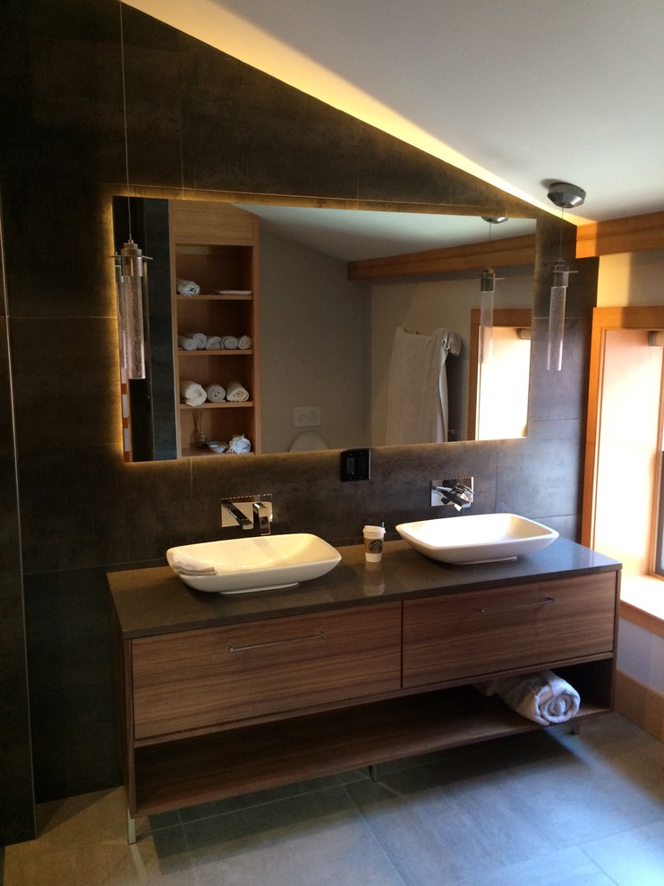 Photo of a medium sized modern ensuite bathroom in Boston with a vessel sink, flat-panel cabinets, medium wood cabinets, engineered stone worktops, a walk-in shower, a wall mounted toilet, grey tiles, ceramic tiles, black walls and ceramic flooring.