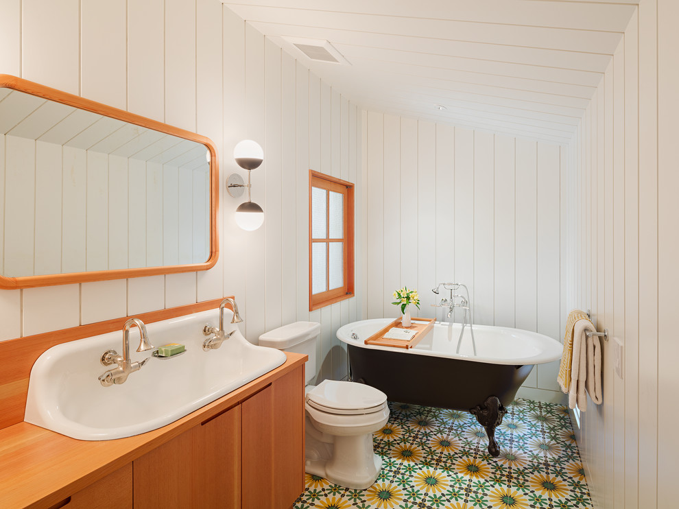 Идея дизайна: ванная комната в стиле кантри с плоскими фасадами, фасадами цвета дерева среднего тона, ванной на ножках, раздельным унитазом, белыми стенами, раковиной с несколькими смесителями, столешницей из дерева, разноцветным полом и зеркалом с подсветкой