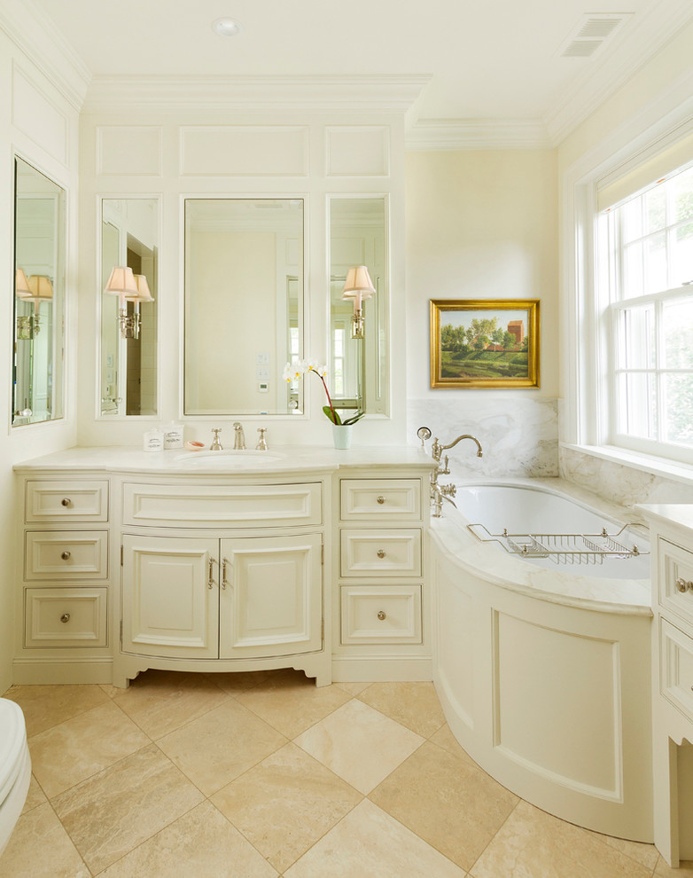 На фото: главная ванная комната среднего размера в классическом стиле с фасадами с декоративным кантом, белыми фасадами, каменной плиткой, мраморной столешницей, полновстраиваемой ванной, бежевой плиткой, желтыми стенами, врезной раковиной и зеркалом с подсветкой с