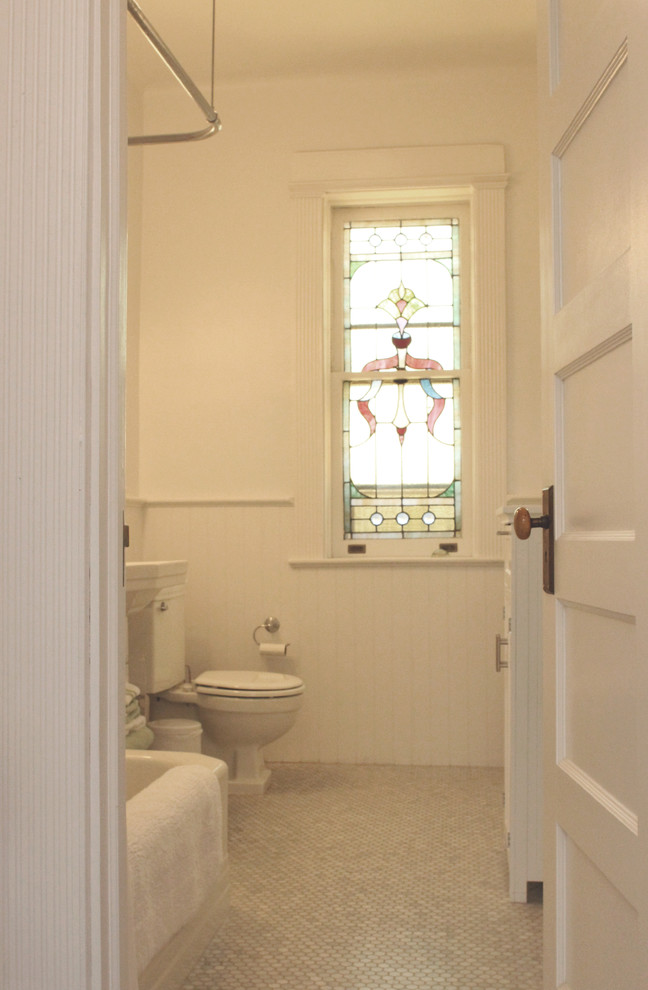 Cette photo montre une salle d'eau chic de taille moyenne avec WC séparés, des portes de placard blanches, une baignoire d'angle, un combiné douche/baignoire, un sol en carrelage de céramique, un lavabo de ferme, un sol gris, une cabine de douche avec un rideau, une fenêtre, meuble simple vasque, meuble-lavabo sur pied et un carrelage blanc.