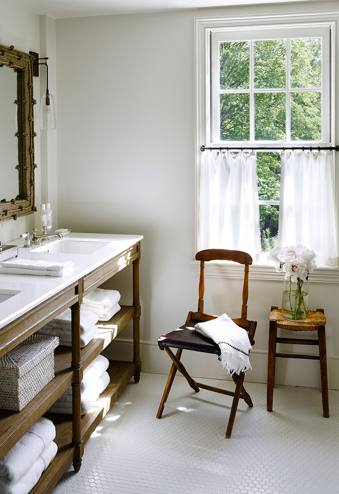 Lantlig inredning av ett badrum, med skåp i ljust trä, ett undermonterad handfat och vita väggar