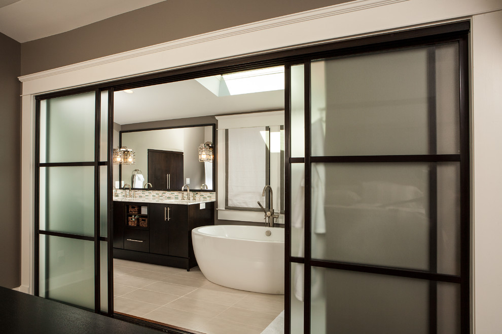На фото: ванная комната в современном стиле с плоскими фасадами, темными деревянными фасадами и отдельно стоящей ванной с