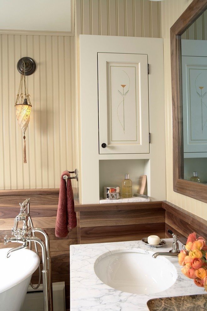 Cette image montre une salle de bain principale rustique avec un lavabo encastré, un plan de toilette en marbre, une baignoire indépendante, un mur beige, un placard avec porte à panneau encastré et des portes de placard blanches.