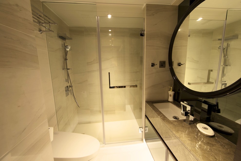 This is an example of a modern shower room bathroom in Hong Kong with marble worktops, beige tiles, a wall mounted toilet, a built-in sink, beige walls and marble flooring.