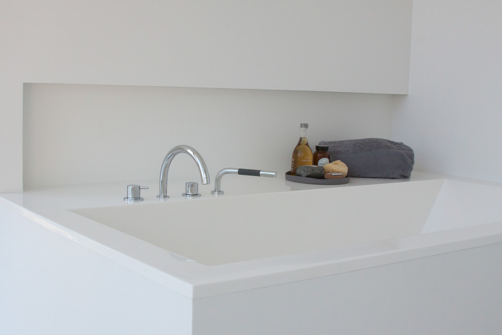 Idee per una stanza da bagno padronale minimal di medie dimensioni con lavabo integrato, ante lisce, ante bianche, top in superficie solida, vasca da incasso, piastrelle bianche, piastrelle in pietra e pareti bianche