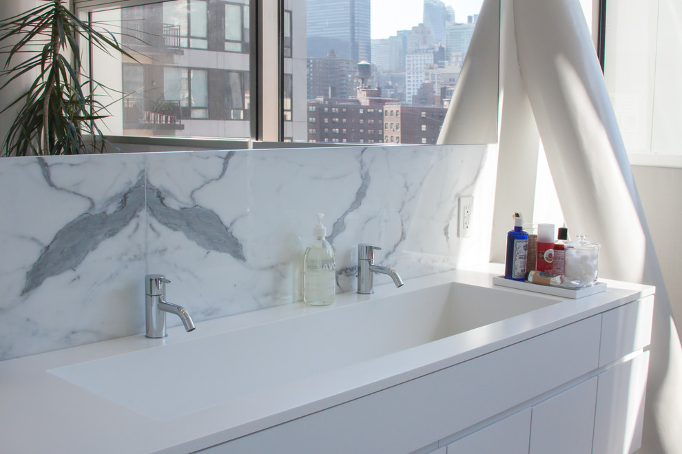 Mittelgroßes Modernes Badezimmer En Suite mit integriertem Waschbecken, flächenbündigen Schrankfronten, weißen Schränken, Mineralwerkstoff-Waschtisch, Einbaubadewanne, weißen Fliesen, Steinfliesen und weißer Wandfarbe in New York