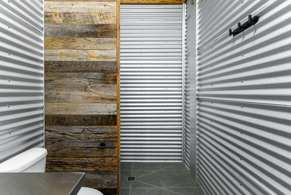 Foto på ett litet industriellt grå badrum, med öppna hyllor, grå skåp, en toalettstol med hel cisternkåpa, grå kakel, kakel i metall, grå väggar, skiffergolv, ett integrerad handfat, bänkskiva i rostfritt stål och grått golv