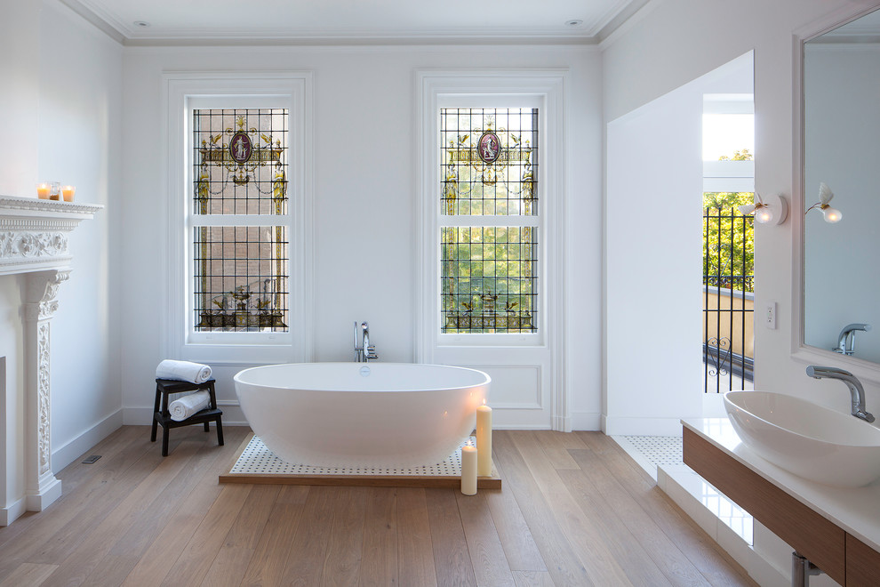Klassisches Badezimmer mit Aufsatzwaschbecken, flächenbündigen Schrankfronten, hellbraunen Holzschränken, freistehender Badewanne, weißer Wandfarbe und braunem Holzboden in New York